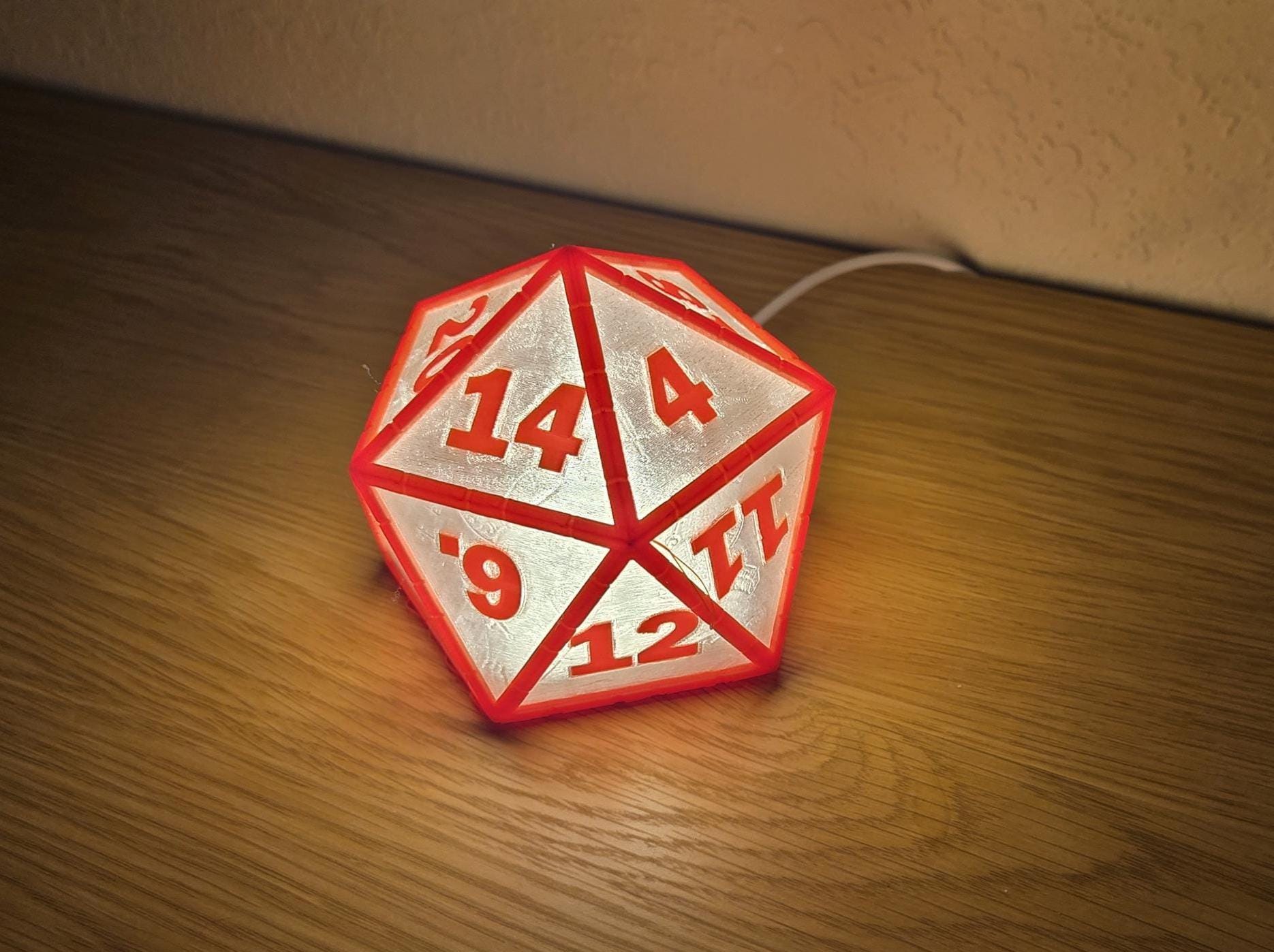 A red and white D20 dice lamp with numbers on each face, placed on a wooden surface.