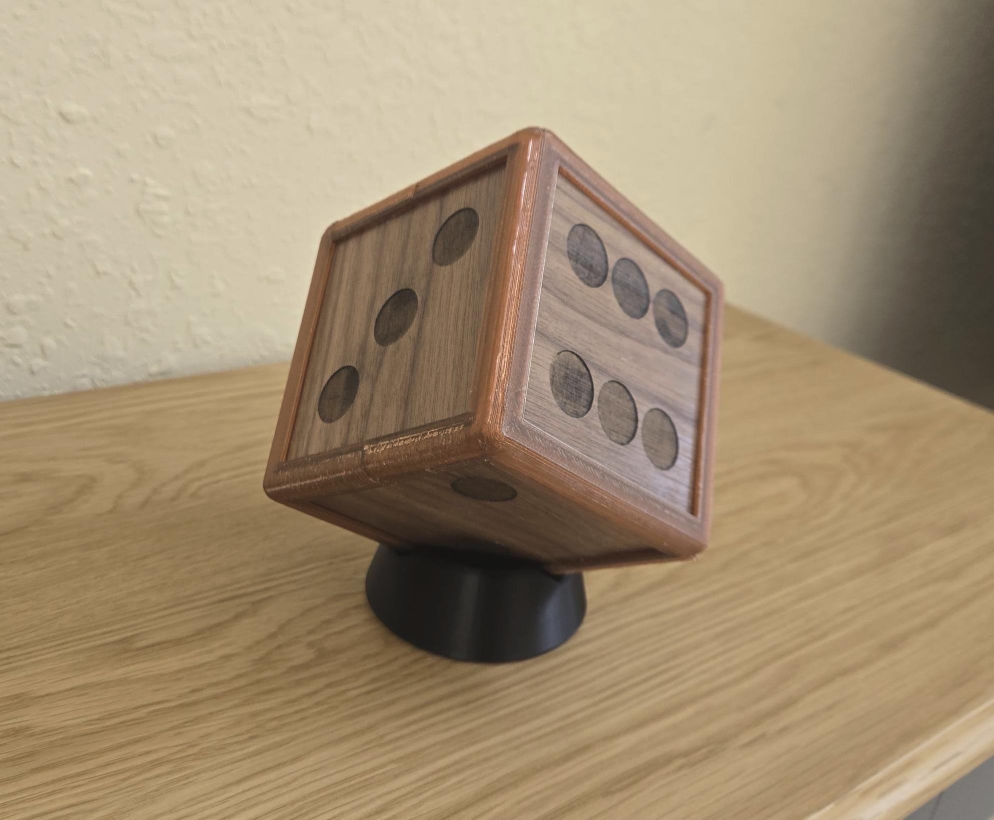 An oversized walnut die with stand, featuring a rich brown color and a textured surface with raised dots, placed on a black.