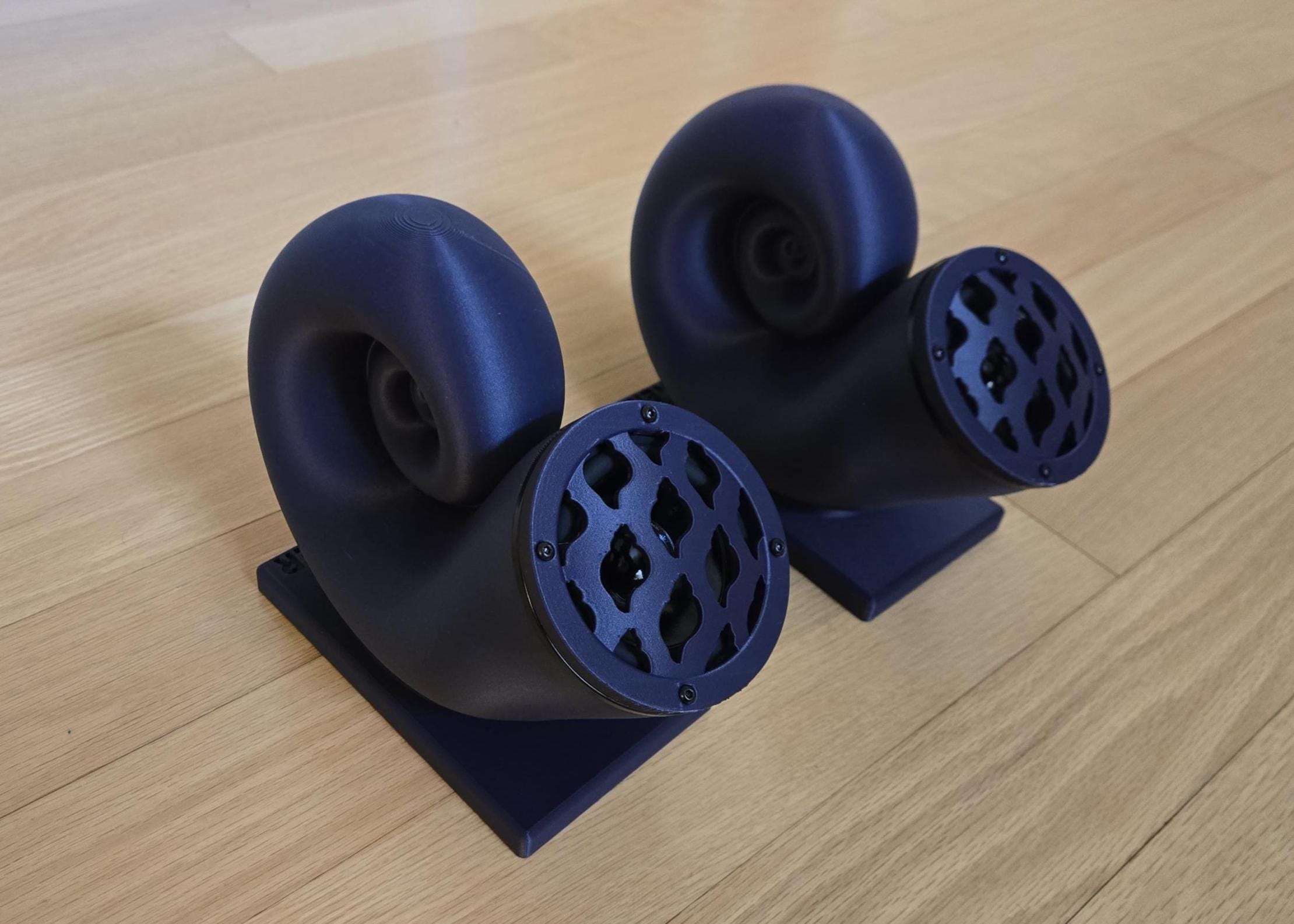 A pair of black Nautilus speakers with a Bluetooth amp, placed on a wooden surface.