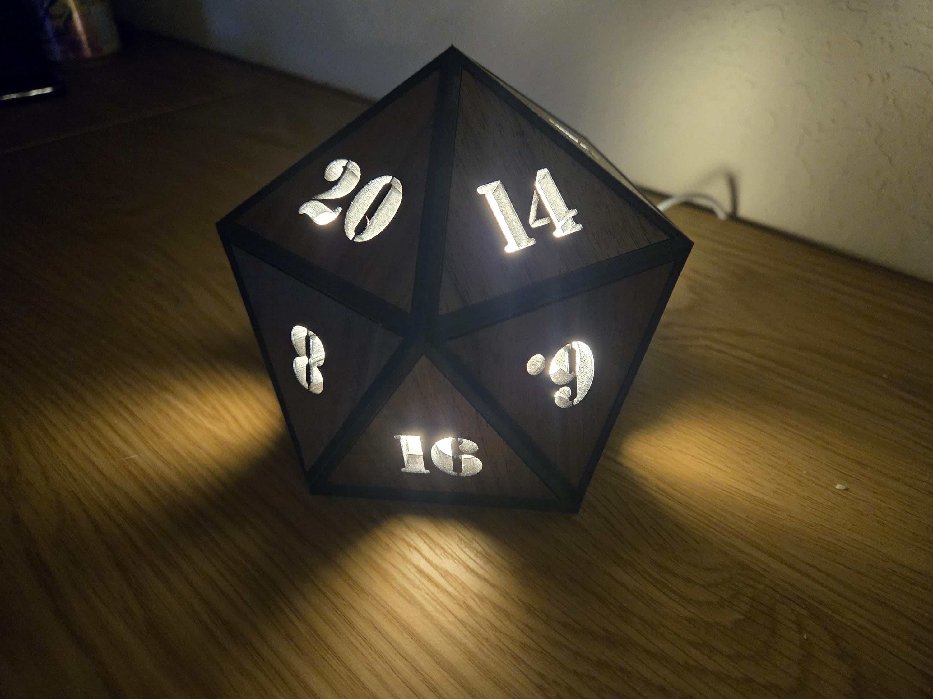 Walnut D20 dice lamp glowing through number cutouts in a dim room, with dark edges outlining triangular wood panels.