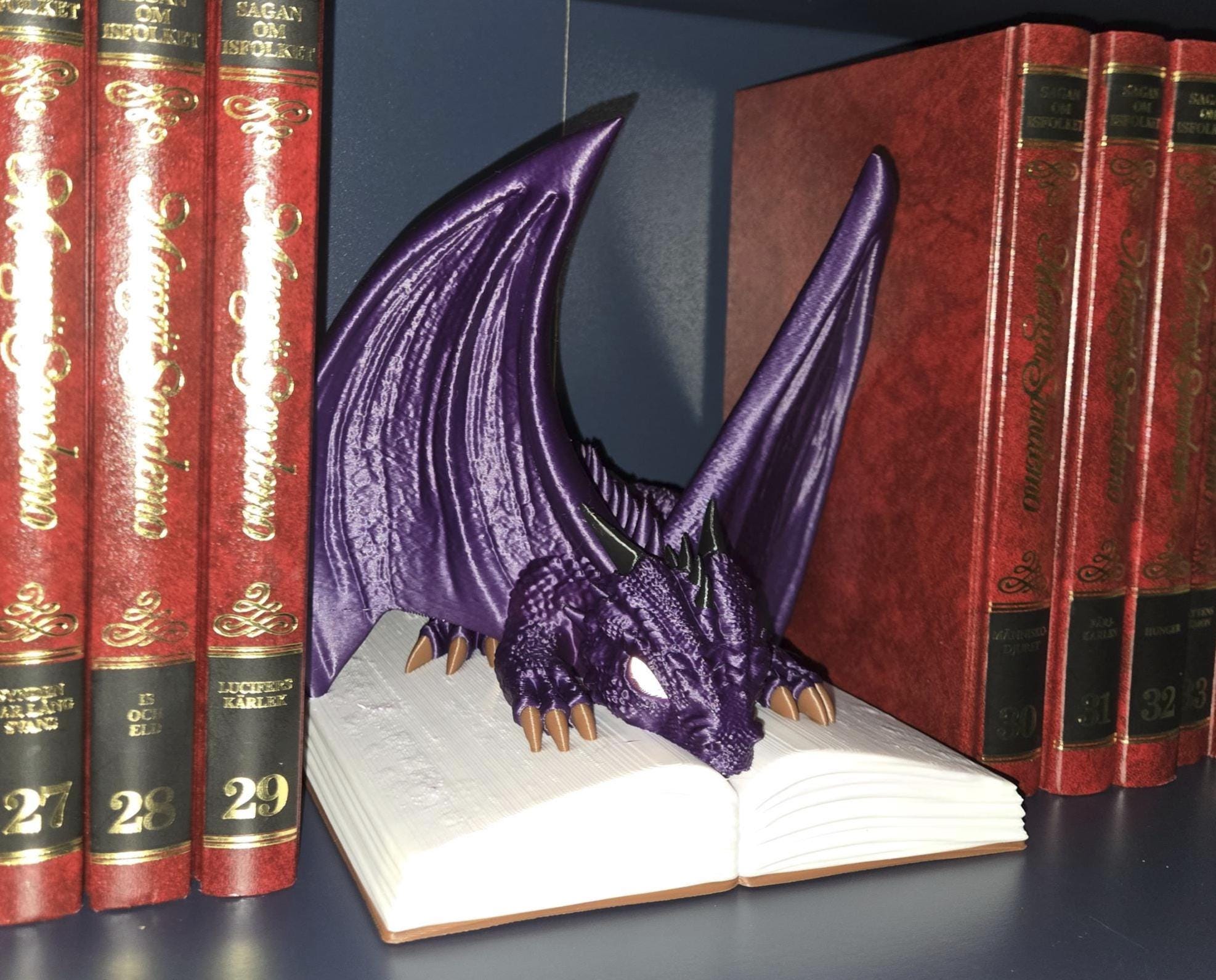 A purple dragon figurine with wings and a tail, perched on an open book, surrounded by red books with gold lettering.