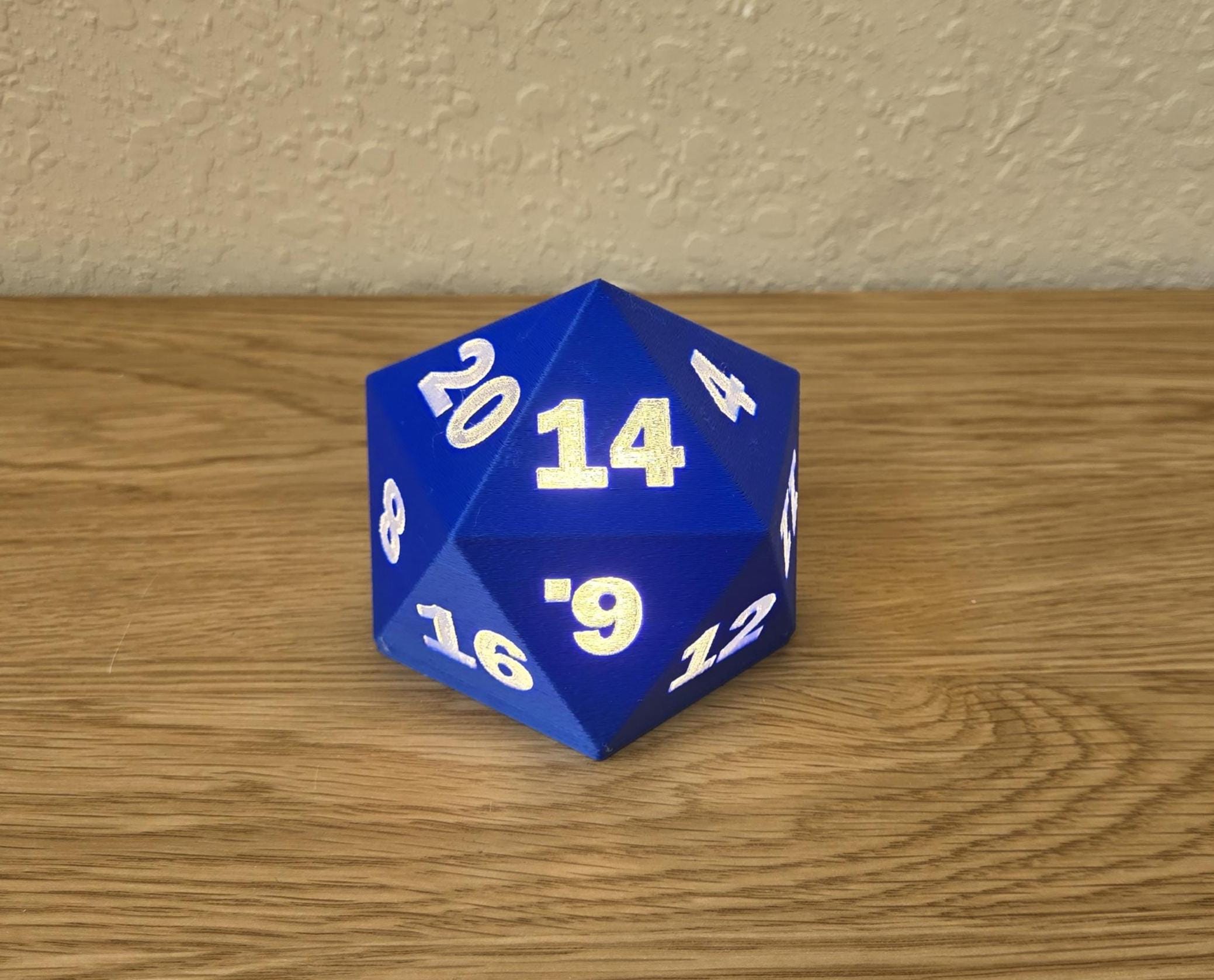 Blue D20 dice lamp on a wooden surface in a bright room, with glowing numbers across its triangular faces.