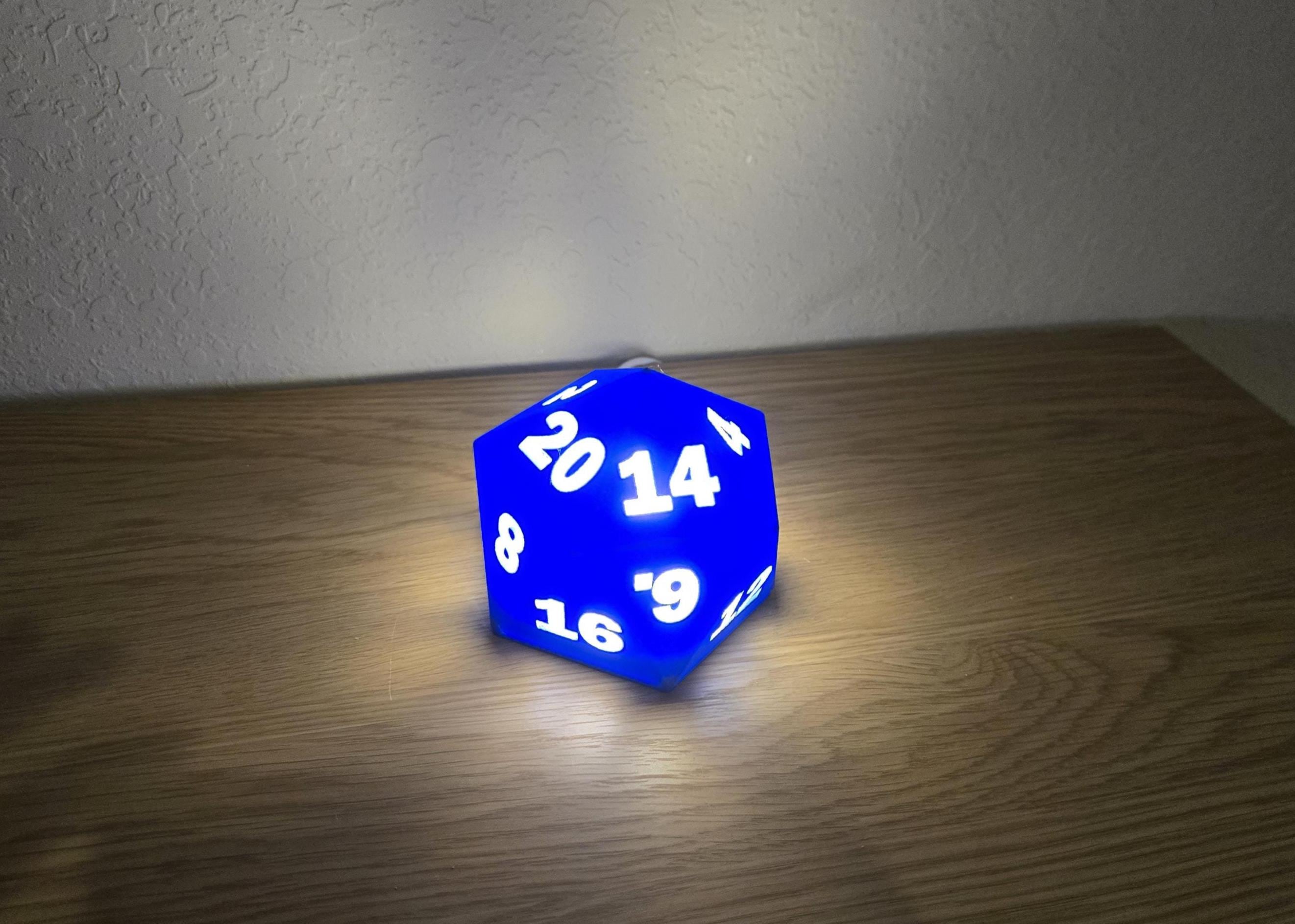 A blue D20 dice night light with white numbers on a wooden surface.