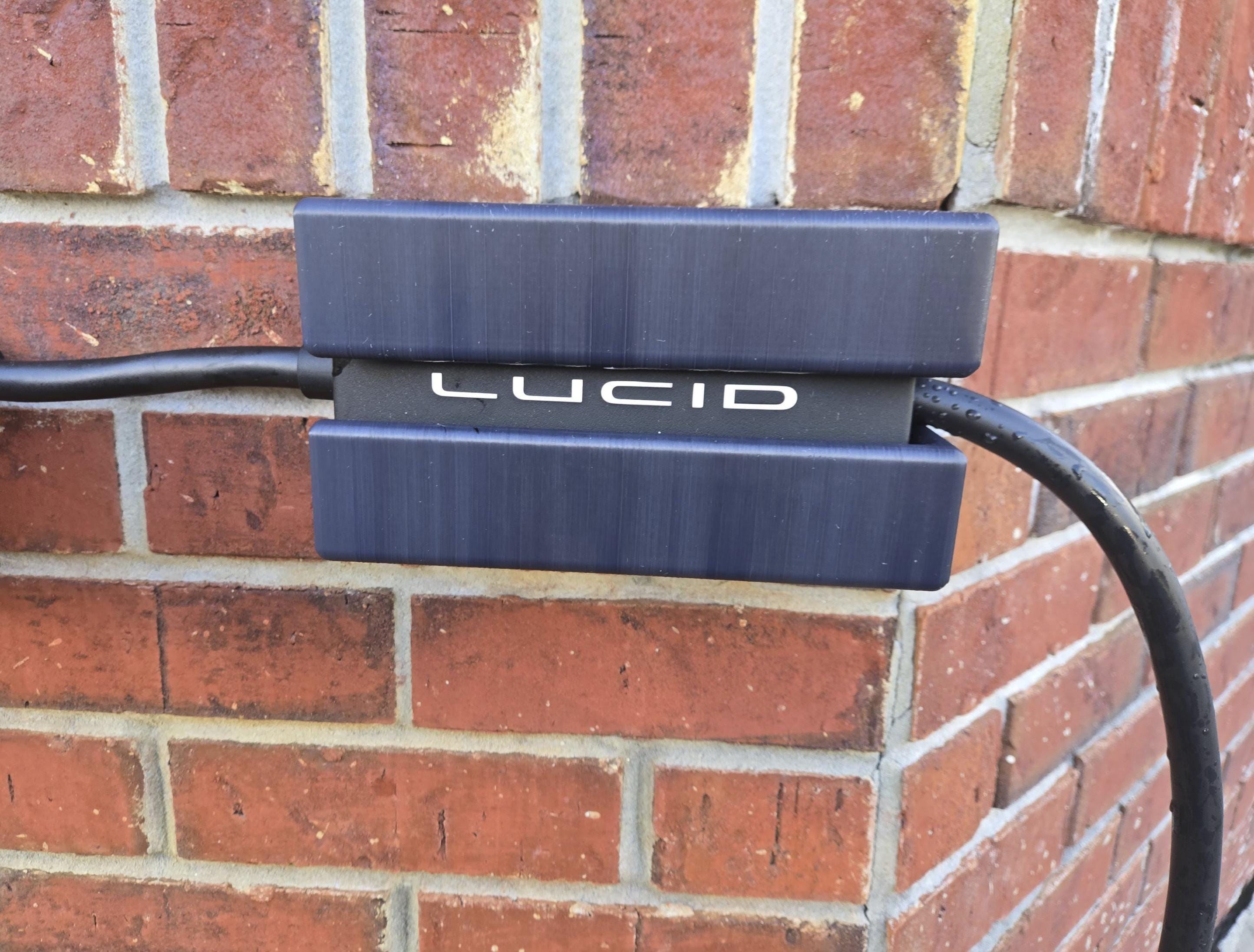 A Lucid charging cable control box holder attached to a brick wall, with the Lucid logo visible on the front panel.