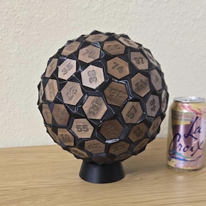 May include: A spherical, geometric sculpture with wooden, numbered tiles set into a black base. The numbers are etched into the wood. A can of La Croix sparkling water is next to the sculpture.