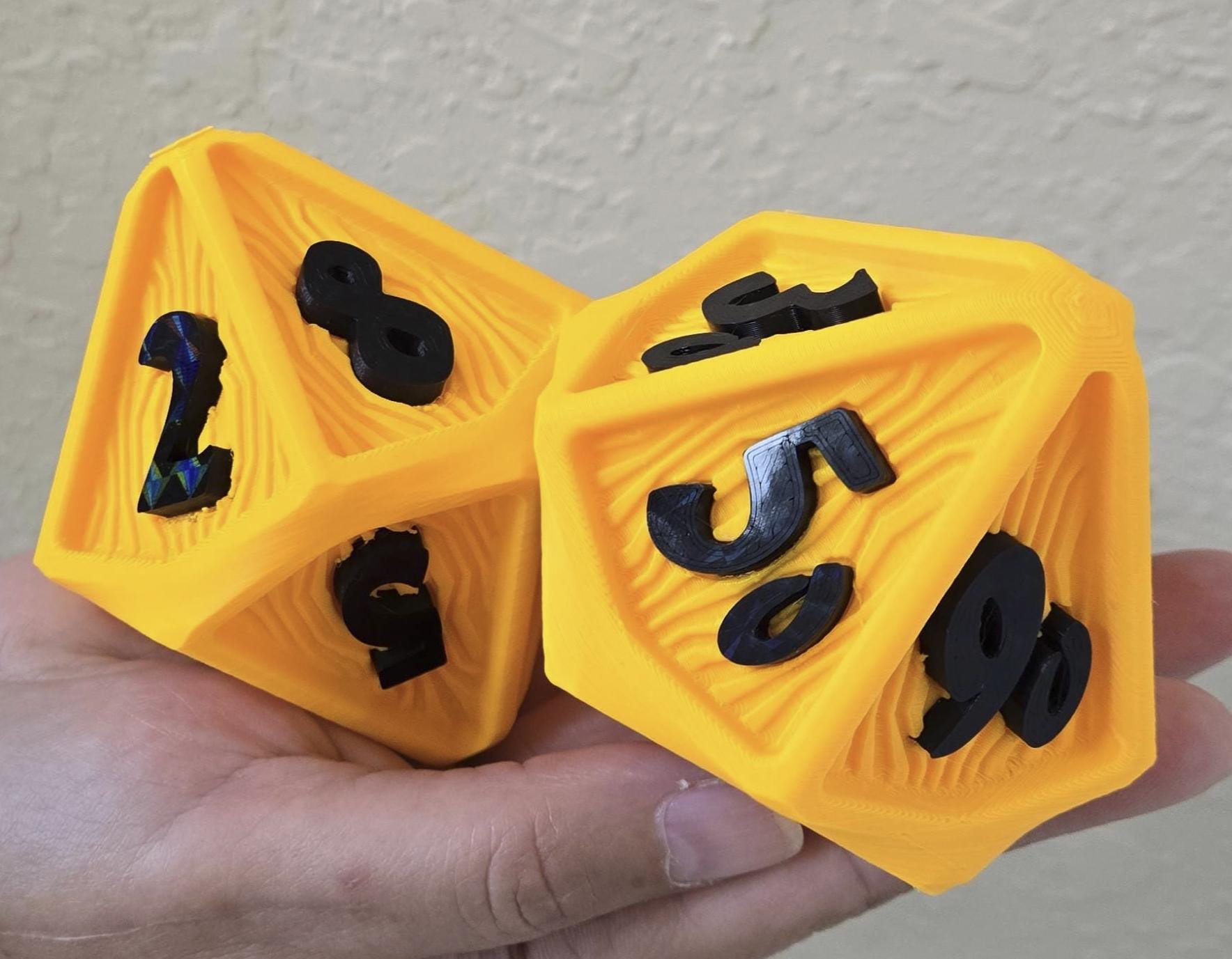 A hand holding two oversized yellow D100 dice with black numbers on them.