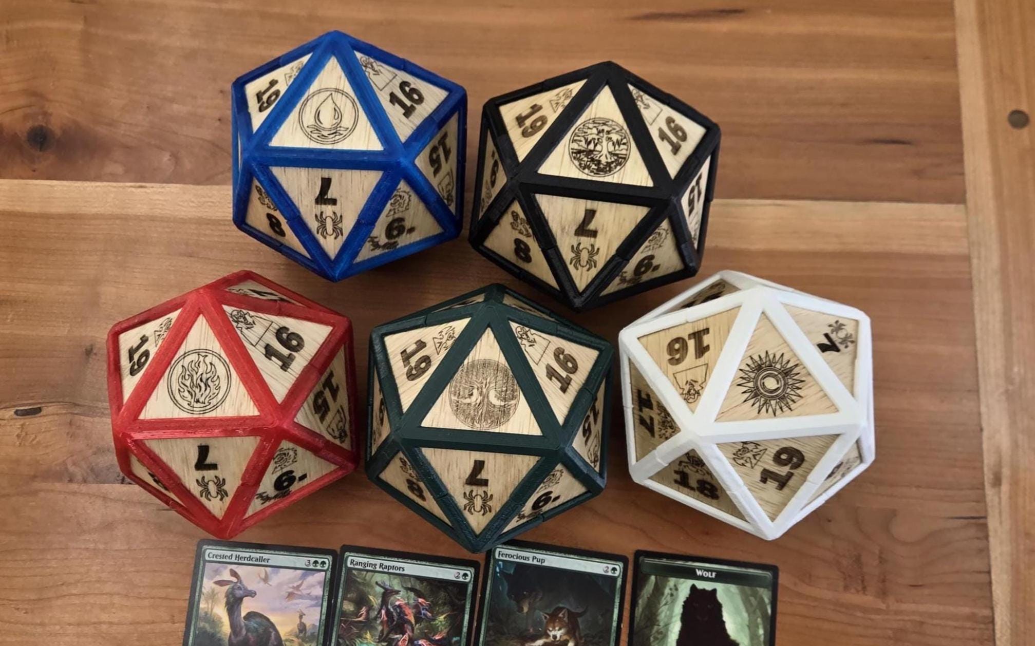 Five wooden D20 spindown dice in various colors and designs, displayed on a wooden surface with four playing cards featuring.