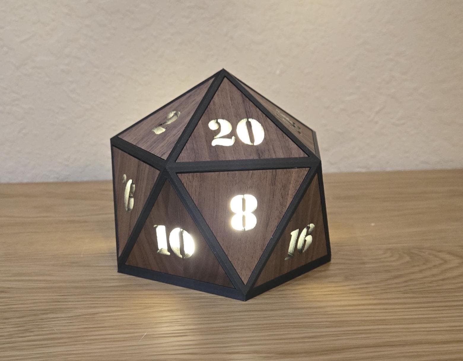 A wooden D20 dice night light with black accents and illuminated numbers on a wooden surface.