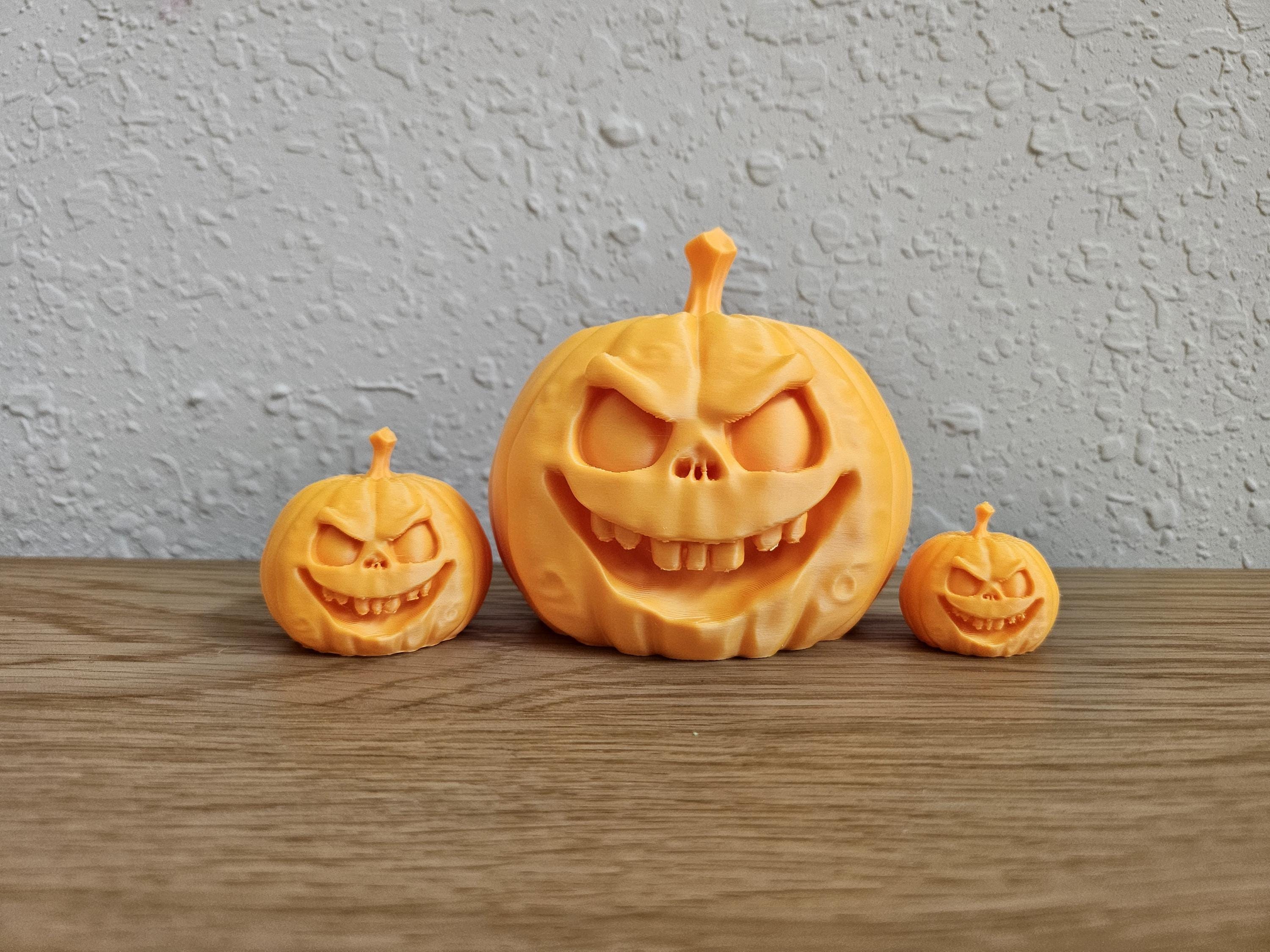Three miniature Jack O Lantern pumpkins with carved faces, displayed on a wooden surface against a textured wall.