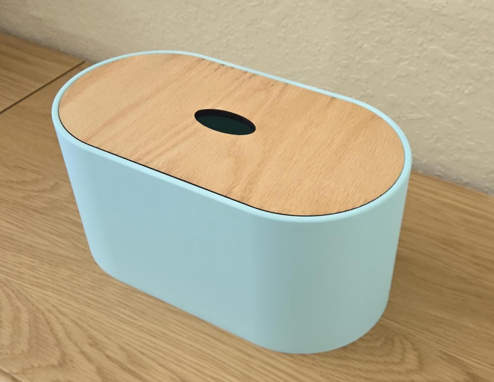 A light blue toilet paper holder with a wooden lid, placed on a wooden surface.