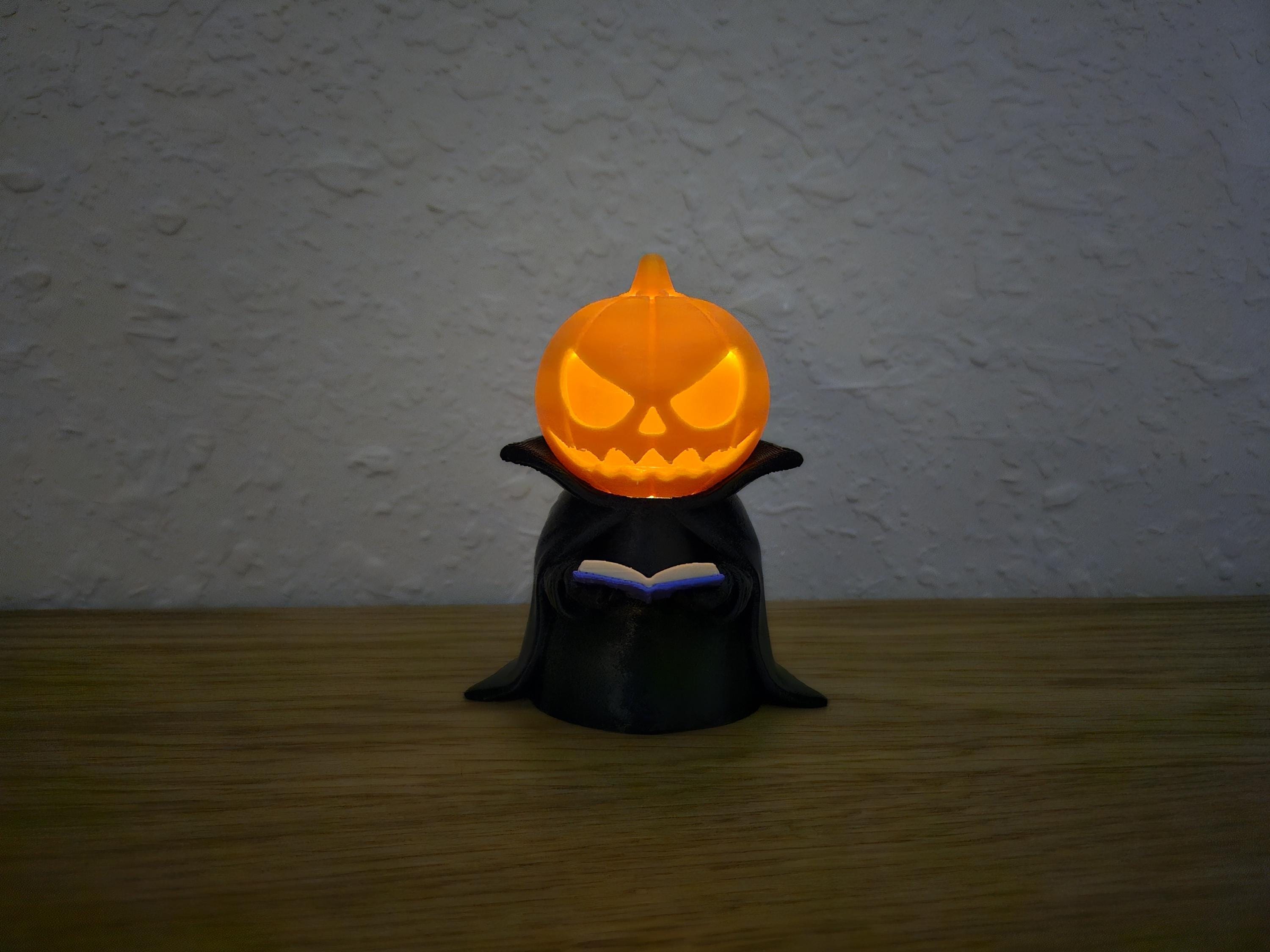 A glowing Jack-o-Lantern figurine with a book in its hands, placed on a wooden surface.