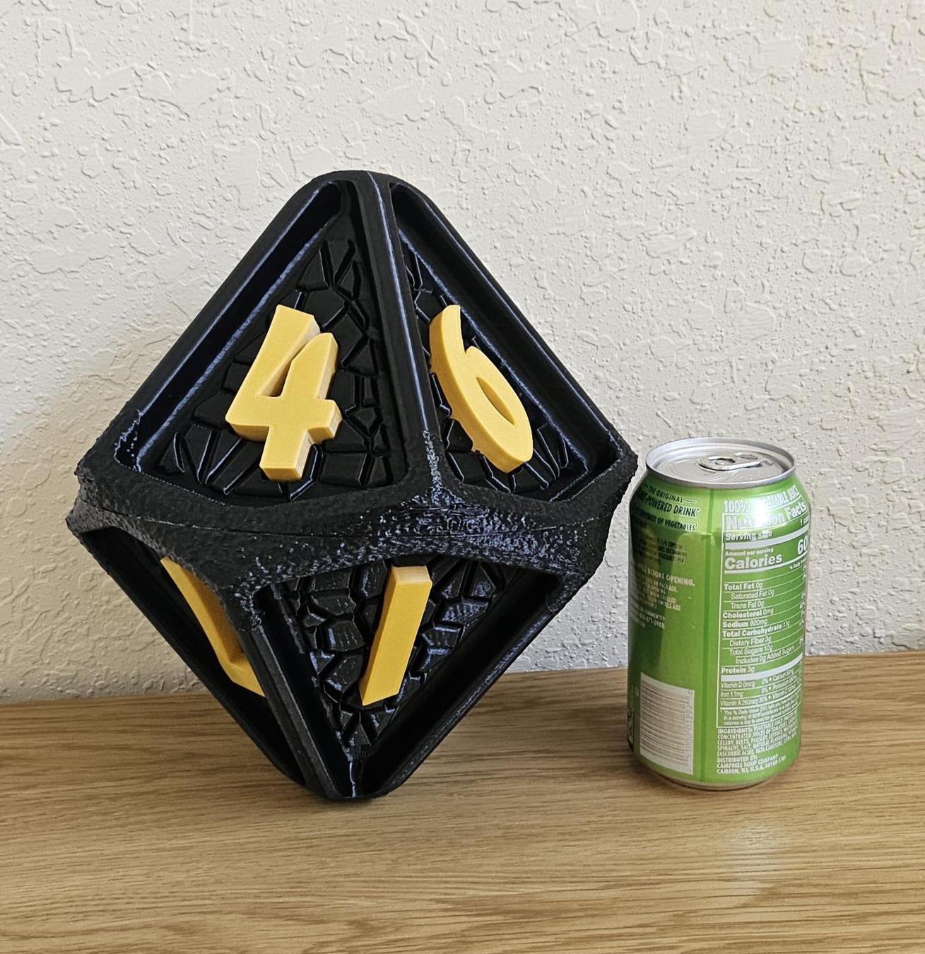 A giant rubberized D10 dice, 9 inches in size, with yellow numbers on a black background, placed next to a soda can for scale.