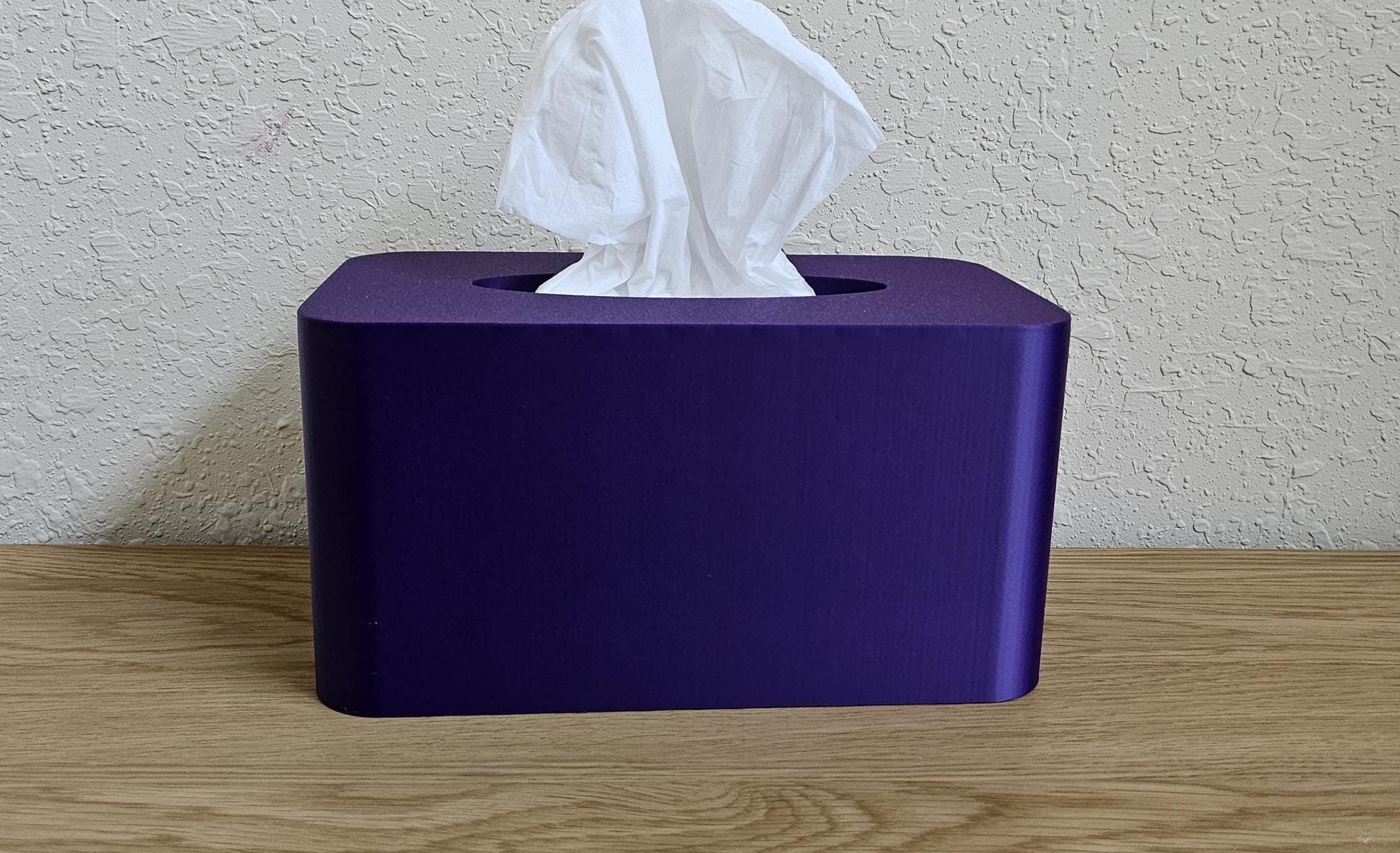 A modern tissue box cover in a deep purple color, holding a pack of Kleenex tissues.