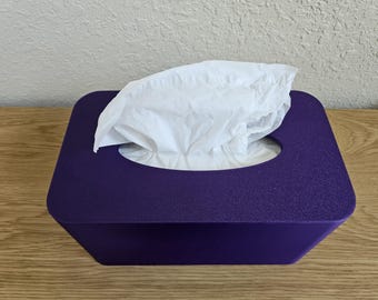 May include: A square, deep purple tissue box with a textured surface. White tissues are overflowing from the oval opening on top. The box is sitting on a light brown wooden surface.