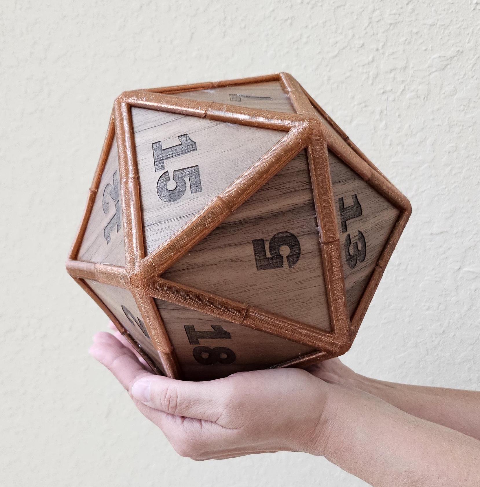 A hand holding a large, wooden D20 dice with rubberized edges, featuring custom engravings and a walnut finish.