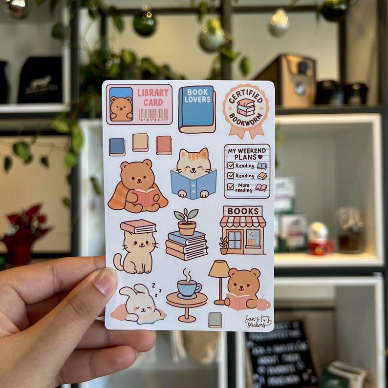 Puede incluir: Una hoja de pegatinas con ilustraciones tem&aacute;ticas de lectura. Los dise&ntilde;os incluyen un oso con un libro, un gato leyendo, un conejito durmiendo y una taza de caf&eacute;. El texto incluye "Library Card", "Book Lovers" y "Certified Bookworm."