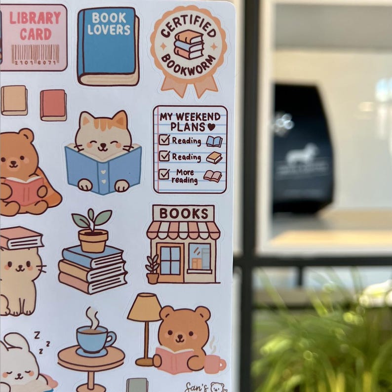 Puede incluir: Una hoja de pegatinas con tem&aacute;tica de lectura. Los dise&ntilde;os incluyen una tarjeta de biblioteca, un libro azul, un gato leyendo un libro, un oso leyendo un libro y el texto "BOOK LOVERS", "CERTIFIED BOOKWORM", "MY WEEKEND PLANS" y "BOOKS".