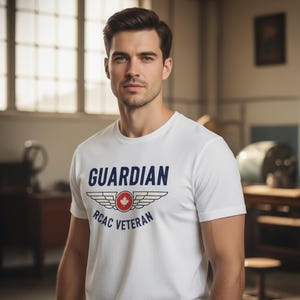 Peut inclure: T-shirt blanc avec le mot "GUARDIAN" en bleu marine, au-dessus d'un motif d'ailes et d'un cercle rouge avec une feuille d'érable. Le texte "RCAC VETERAN" est en dessous. Le t-shirt est porté par une personne.
