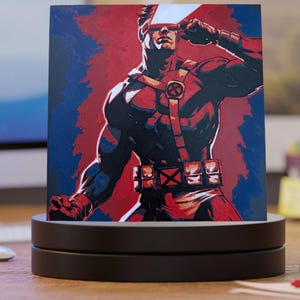 May include: A square print of a comic book character, Cyclops, in a dynamic pose. The artwork features a red and blue color scheme with the character wearing a red and black uniform. The print is displayed on a black rotating stand.