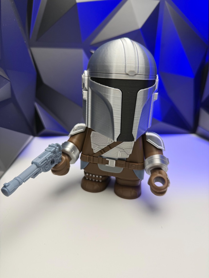 May include: A stylized figure of The Mandalorian, featuring a silver helmet and armor, brown clothing, and a gray blaster. The figure is posed against a blue and black geometric background.