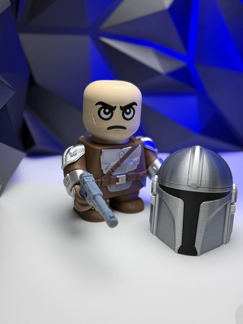 May include: A 3D-printed action figure of a character with a stern expression, wearing brown armor, a silver pauldron, and holding a light blue blaster. A silver helmet is placed next to the figure. The background is a geometric blue design.