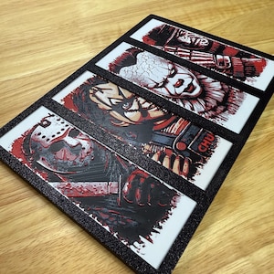 May include: A black framed artwork with four horror film character portraits. Each portrait is in red, black, and white, with a textured finish. The characters include Jason Voorhees, Chucky, and Pennywise.