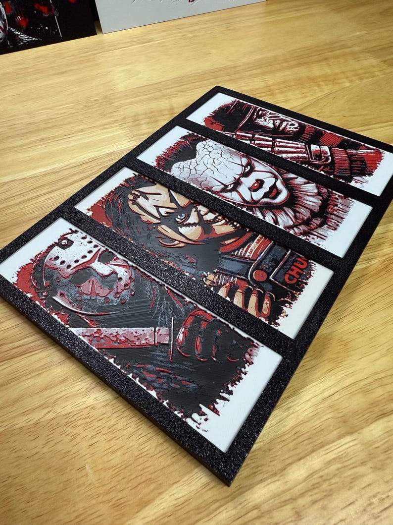 May include: A black framed artwork with four horror film character portraits. Each portrait is in red, black, and white, with a textured finish. The characters include Jason Voorhees, Chucky, and Pennywise.