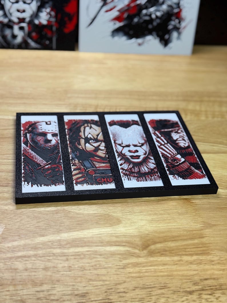 May include: A black rectangular decorative item featuring four horror movie characters: Jason Voorhees, Chucky, Pennywise, and Freddy Krueger. Each character is depicted in a vertical panel with a red and black colour scheme. The item is displayed on a wooden surface.