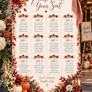 Puede incluir: Un cartel de distribución de mesas de boda con el texto Please Find Your Seat, una lista de doce mesas con nombres de invitados y la frase Good Company Brighter Days. El cartel está decorado con hojas de otoño, flores y un gran lazo marrón.