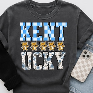 Puede incluir: Sudadera gris oscuro con la palabra "KENT" en letras a cuadros azules y blancos. Debajo de la palabra "KENT" hay cinco figuras de gatos de dibujos animados. La palabra "UCKY" está debajo, con un estampado floral azul.