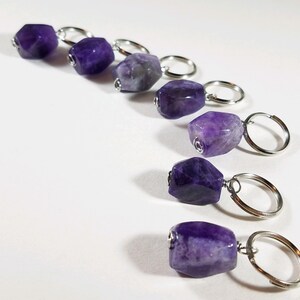 May include: Seven amethyst gemstone stitch markers with silver rings. The amethyst stones are various shades of purple and have a faceted, irregular shape.