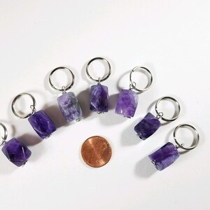 May include: Eight amethyst stone keychains with silver rings. The stones are faceted and have a purple and white color. A penny is included for size reference.
