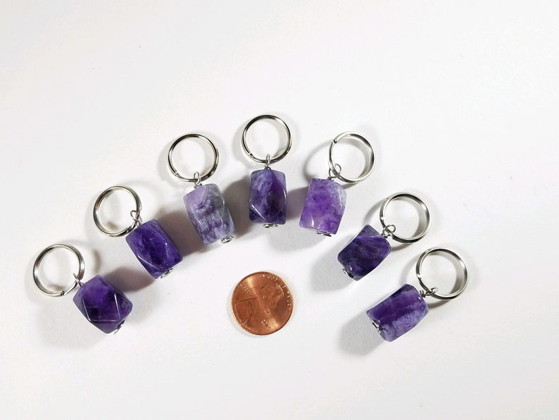 May include: Eight amethyst stone keychains with silver rings. The stones are faceted and have a purple and white color. A penny is included for size reference.