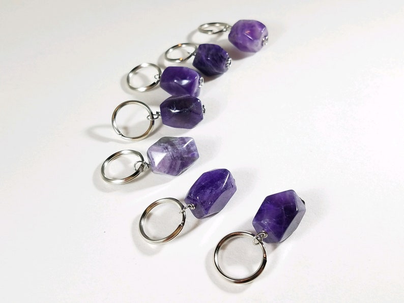 May include: Seven amethyst stone keychains with silver key rings. The amethyst stones are various shades of purple and have a faceted, geometric shape.