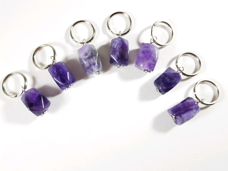 May include: Seven amethyst gemstone stitch markers with silver rings. The amethyst stones are faceted and have a purple and white color.
