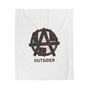 Pode incluir: Cobertor branco com um design circular. O design apresenta a letra "A" dentro de um círculo, feito de tecido xadrez em tons de bordô, verde e amarelo. A palavra "OUTSIDER" é impressa em preto abaixo.