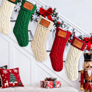 Könnte beinhalten: Personalisierte Weihnachtsstrümpfe in Creme, Grün und Rot, die an einer Treppe hängen. Jeder Strumpf hat ein Namensschild aus Leder. Dekorative Kissen und eine Geschenkbox sind ebenfalls zu sehen.