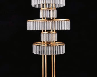 May include: A tiered gold metal stand featuring three circular levels adorned with hanging clear rectangular glass prisms. The structure is supported by vertical gold rods connected to a circular base, creating a multi-layered display piece.