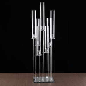 May include: A clear acrylic candelabra with multiple candle holders. The candelabra has a rectangular base and several vertical tubes of varying heights. The candle holders are designed to hold small candles. The background is black.