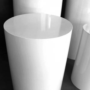 May include: A collection of white cylindrical pedestals of varying heights. The pedestals have a glossy finish and a smooth, rounded top. The arrangement suggests a display or staging setup, with the objects casting subtle reflections.