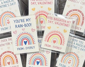 May include: A set of eight Valentine's Day cards featuring rainbow designs with the text "You're my rain-boo!" and "You brighten my day, Valentine!"  Each card has a rainbow with a heart in the center and the text "From: Everly".