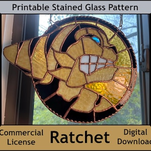 Può includere: Un modello di vetro colorato di un personaggio Ratchet giallo e nero con un occhio blu. Il modello è incorniciato in rame ed è pronto per essere stampato per un progetto di vetro colorato.