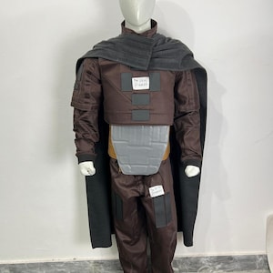 May include: A brown costume with a gray cape and accents. The costume includes a jacket, pants, and a chest piece. The text "The Deal Digger" is visible on the costume. The mannequin is wearing white shoes.