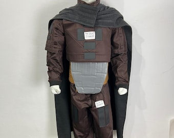 May include: A brown costume with a gray cape and accents. The costume includes a jacket, pants, and a chest piece. The text "The Deal Digger" is visible on the costume. The mannequin is wearing white shoes.