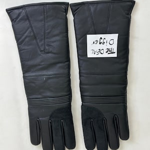 May include: A pair of black leather gloves with long gauntlets. The gloves have a textured appearance and feature a suede-like material on the palms and fingers. The text "THE DEAL D199er" is visible on a white label.
