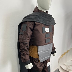 May include: A brown costume with a gray cape and accents, displayed on a mannequin. The costume includes a jacket, pants, and a belt. The text "The Deal Digger" is visible on the costume.