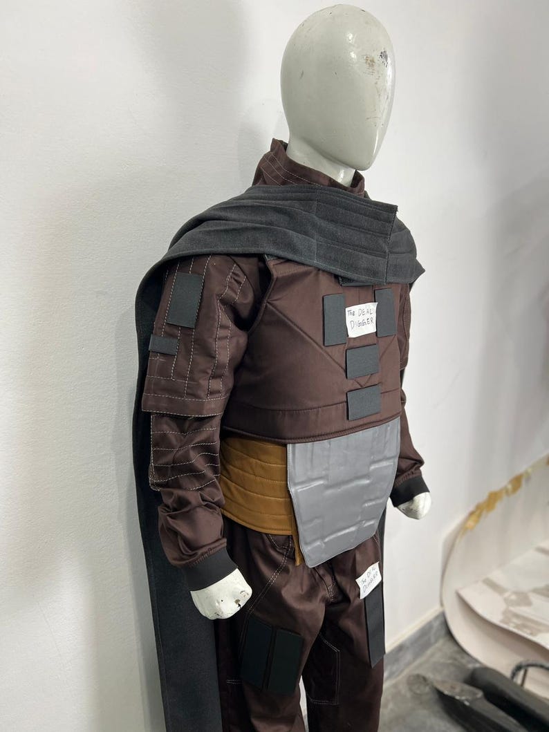 May include: A brown costume with a gray cape and accents, displayed on a mannequin. The costume includes a jacket, pants, and a belt. The text "The Deal Digger" is visible on the costume.