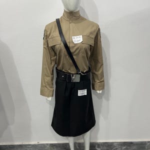 Könnte beinhalten: Outfit aus einem beigefarbenen langärmligen Hemd und einem schwarzen Rock, präsentiert auf einer Schaufensterpuppe. Das Hemd hat einen hohen Kragen und zwei Brusttaschen. Ein schwarzer Gürtel und ein Schulterriemen sind enthalten. Der Text "The Deal Digger" ist sichtbar.