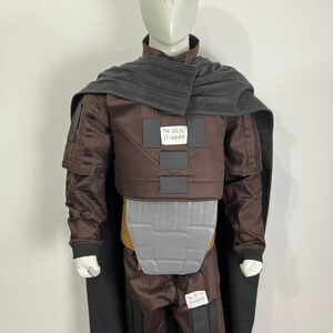 May include: A brown costume with a gray cape and accents, displayed on a mannequin. The costume includes a jacket, pants, and a chest plate. The text "THE DEAL DIGGER" is visible on the costume.