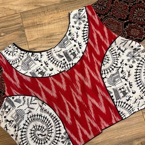 May include: A red and white cotton blouse with a black and white geometric pattern. The blouse has a round neckline and three-quarter sleeves.